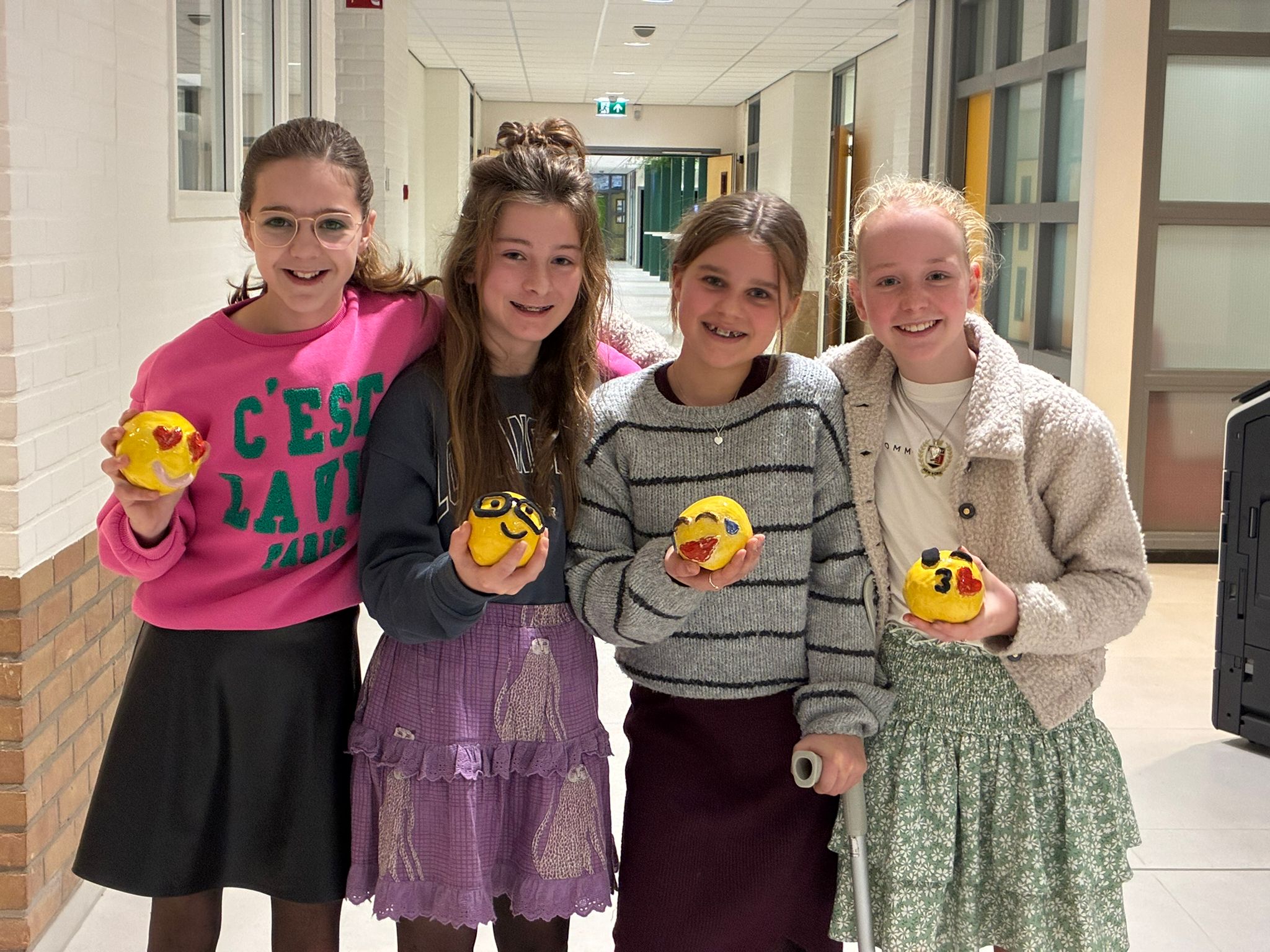 Vier leerlingen tonen hun zelfgemaakte emoji's van klei